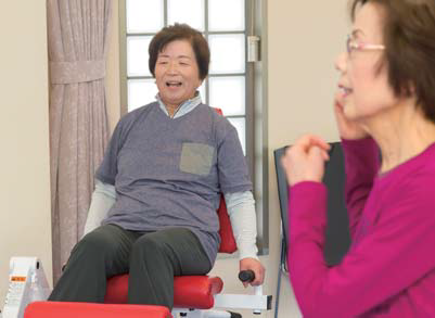 器具を使って運動するカズ子さんと、恵子さんの横顔の写真