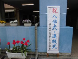 祝入学式・進級式と書かれた縦看板の横にプランタに植えられた花々が飾られている写真
