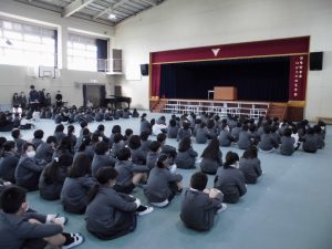 体育館の床に膝を抱えるように座った生徒達の写真