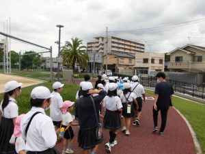 整備された芝生の間にある遊歩道を生徒たちが園児と手を繋ぎ引率の先生と一緒に歩いている写真