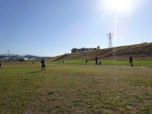 青空の下、緑の芝生が広がった河川敷で遊んでいる生徒たちの写真