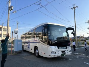 校門前で大型バスを見送っている先生や関係者の方々の写真