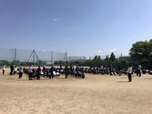 青空の下、おさない はしらない しゃべらない もどらないの規則を守りながら、広い運動場に整列した生徒達の避難訓練の様子を撮影した写真