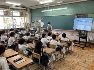 教室内に設置されたテレビモニター画面に、歯磨きについて説明を自席に座り熱心に話を聞く生徒達を右斜め後ろから撮影した写真