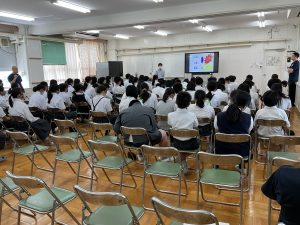 室内に設置されたテレビモニターを使い、設置されたパイプ椅子に座りながら非行防止動画を真剣に見ている様子を背後から撮影した写真