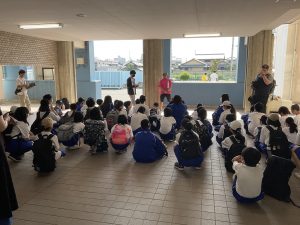 クリーム色と水色を基調とした校舎内で、膝を抱えるように座り熱心に話を聞く生徒達と、向かい合わせで話をされる先生方を背後から撮影した写真