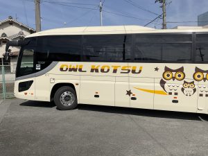 クリーム色の車体側面に、アルファベットでOWL KOUTSUと3羽のフクロウのイラストが描かれたアウル交通のバスを横から撮影した写真