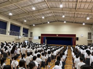 体育館で全校生徒が壇上に向かって整列をしている様子を背後から撮影した写真