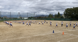 先生方が見守る中、運動場を広く使い生徒たちが学園エイサーの練習をしている写真