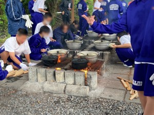 生徒たちが軍手をはめてかまどに火をおこし、鍋をのせて調理をしている様子を写した写真