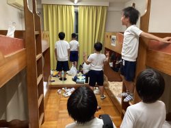 2段ベッドが両側に設置されている部屋で、体操服姿の子どもたちが窓の方向を向いて立っている写真