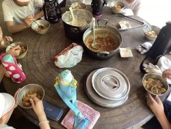 白ご飯とカレーがそれぞれ大きな鍋に入ってテーブル中央に用意されており、自分のお皿に入ったカレーを子どもたちが食べている様子の写真