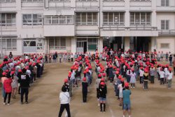 校庭にたくさんの子どもたちが整列して集まっており、校舎側の方には背の小さな子どもたちが横一列になって向かい合うように立っている写真