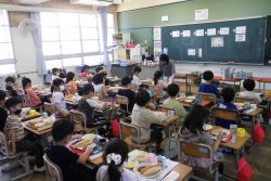 ランチマットの上に給食を並べて椅子に着席している子どもたちを後ろから撮った写真