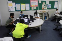 丸いテーブル上で、パソコンのような機器を開いて画面を見ている子どもたちの写真