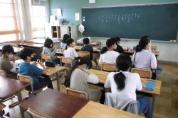 机に筆記用具のようなものを置いて、椅子に座っている子どもたちの写真