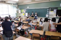 教室で、2名の子どもが椅子から立ち上がっており、教室内のみんなから注目されている様子の写真