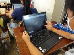机の上にタブレットを置いて、右手の指を使いながら画面を操作している様子の子どもの写真