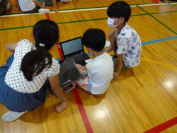 床に座ってタブレットを開いている1名の子どもと、両側に座っている2名の子どもたちの写真