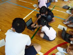 床にタブレットを置いてキーボードを押す子どもと、その横に座ってサポートをしている様子の子どもの写真
