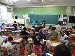 着席している子どもたちや周囲に立っている子どもたちで賑わっている様子の教室内の写真