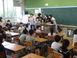 教室に着席している子どもたちや、教卓の周囲に集まった8名ほどの子どもたちが向き合っている写真