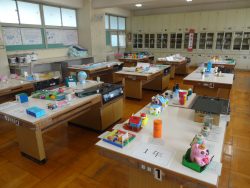 大きなテーブルが等間隔に設置された部屋で、数多くの作品がテーブル上に展示されている写真
