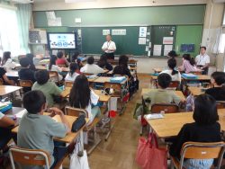 モニターが用意された教室で、着席した子どもたちが、正面にいる関係者の方を見ている写真