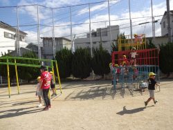 校庭のジャングルジムに上るたくさんの園児たちと、遊具の周りに立っている園児や関係者の写真