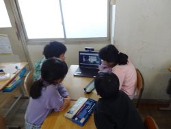 机に一つのタブレットが置かれており、机を挟んで一緒にタブレット画面を見つめている4名の子どもたちの写真