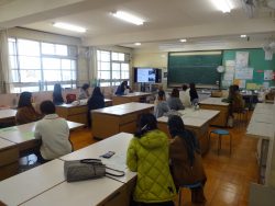 大きなテーブルが等間隔に設置された部屋に保護者の方々が着席しており、設置された大きなモニターの画面を見ている写真