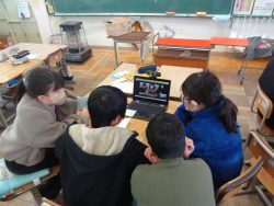机の上に置かれたタブレットの前に4名の生徒が座っており、一緒に画面を見ている写真