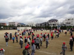 校庭にたくさんの子どもたちが集まり、列を作って数か所でグループができている様子の写真