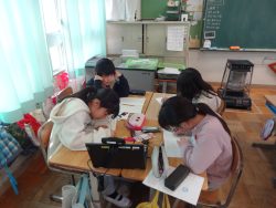 4名の子どもが向かい合わせに着席してノートに文字を書き込んでいる様子の写真