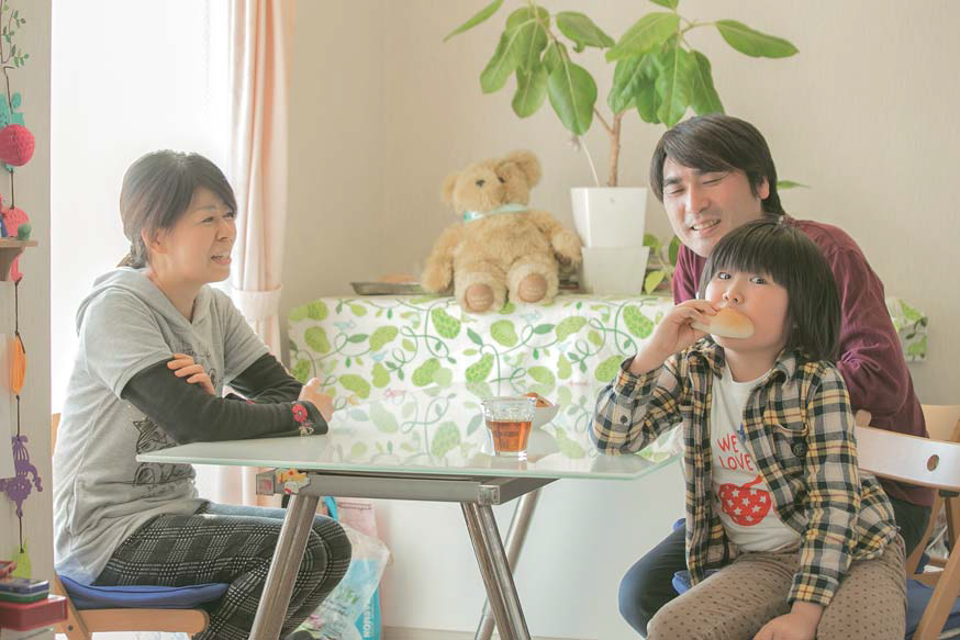 けいらくんがパンを頬張る姿を、笑顔で見ている牟田卓司さんと敦子さんの家族写真