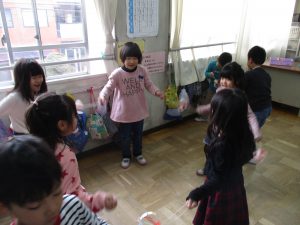 教室で5人程のグループに分かれ、輪になり、ぶんぶんごまを手に持ち回している子供たちの写真