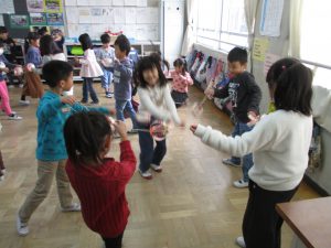 教室で5人ほどのグループに分かれ、ぶんぶんごまを楽しそうに回している子供たちの写真