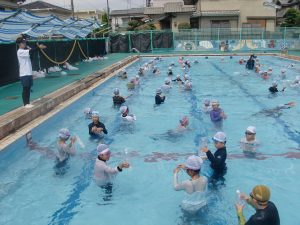 子どもたちは胸ほどまで水の深さがあるプールに友達と間隔をあけて入っており、プールサイドに立つ先生の指導の下、水泳の授業が行われている様をあけて