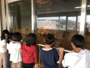 大きなごみクレーンで沢山のごみが運ばれている様子を見渡せる大きな窓越しから見学している子どもたちを写した写真
