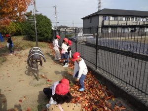 遊具の近くの落ち葉が集まっている周りで生徒たちが袋を手に作業をしている写真