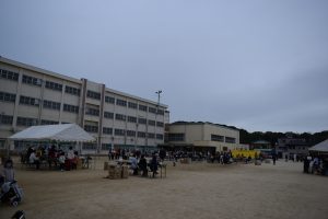 テントや長テーブルが設置された校庭に、たくさんの参加者で賑わっている様子の写真