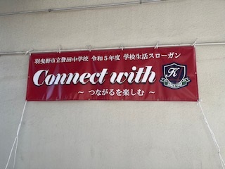 羽曳野市立誉田中学校 令和5年度 学校生活スローガン「Connect with ～つながることを楽しむ～」と書かれたえんじ色の横断幕が掲げられている写真