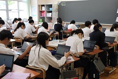 教室の自席に座っている生徒の皆さんがそれぞれタブレット端末を使って学習しているクラス全体の様子を後方から写した写真