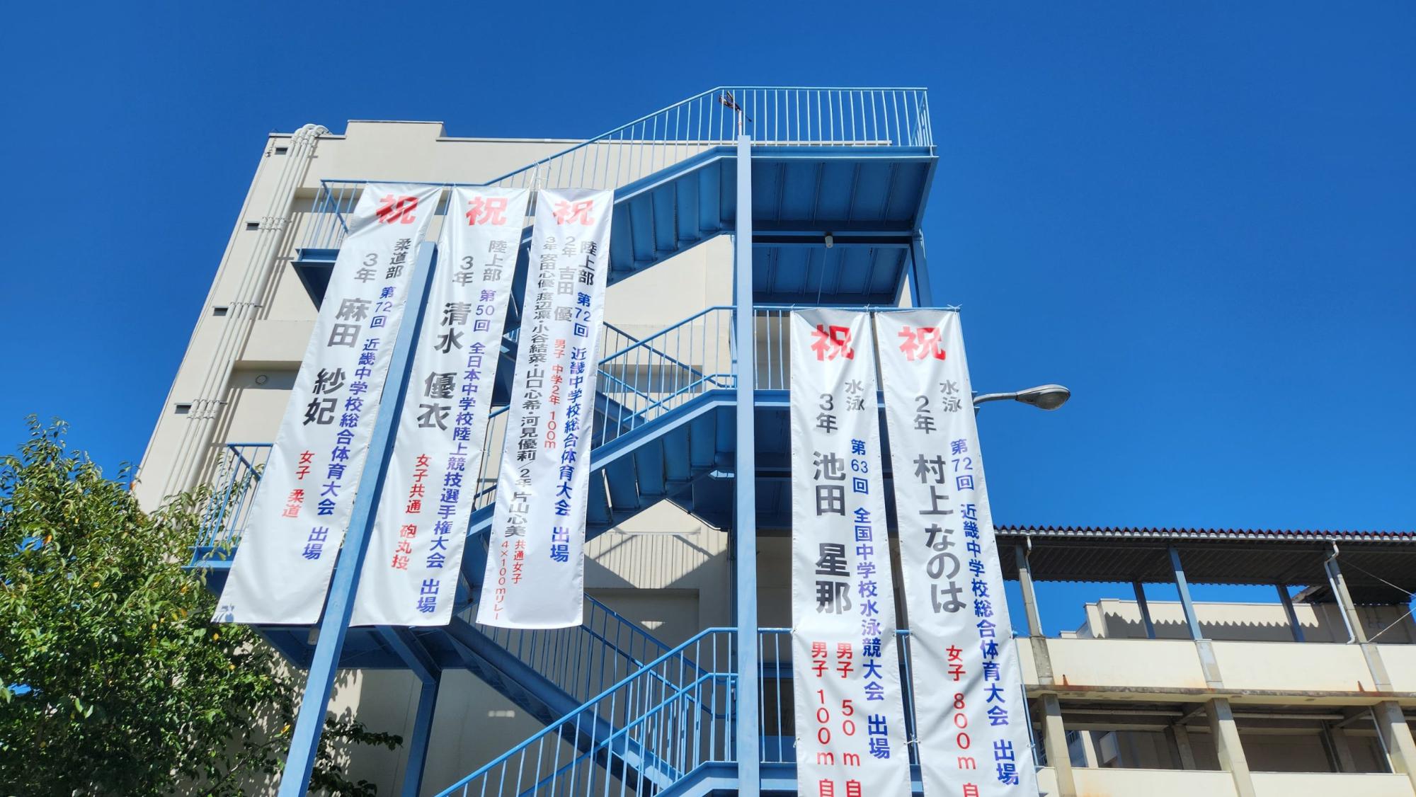 4階の非常階段に陸上部と柔道部、3階の非常階段に水泳部の懸垂幕が飾られている写真
