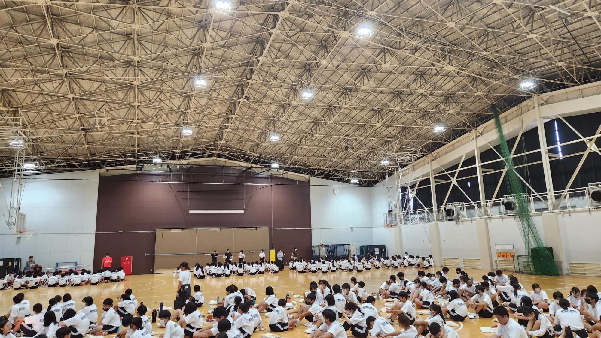 体育館に体操着姿の2年生の生徒たちが集まり、前方に3か所に分かれて座り招集の練習が行われている様子の写真