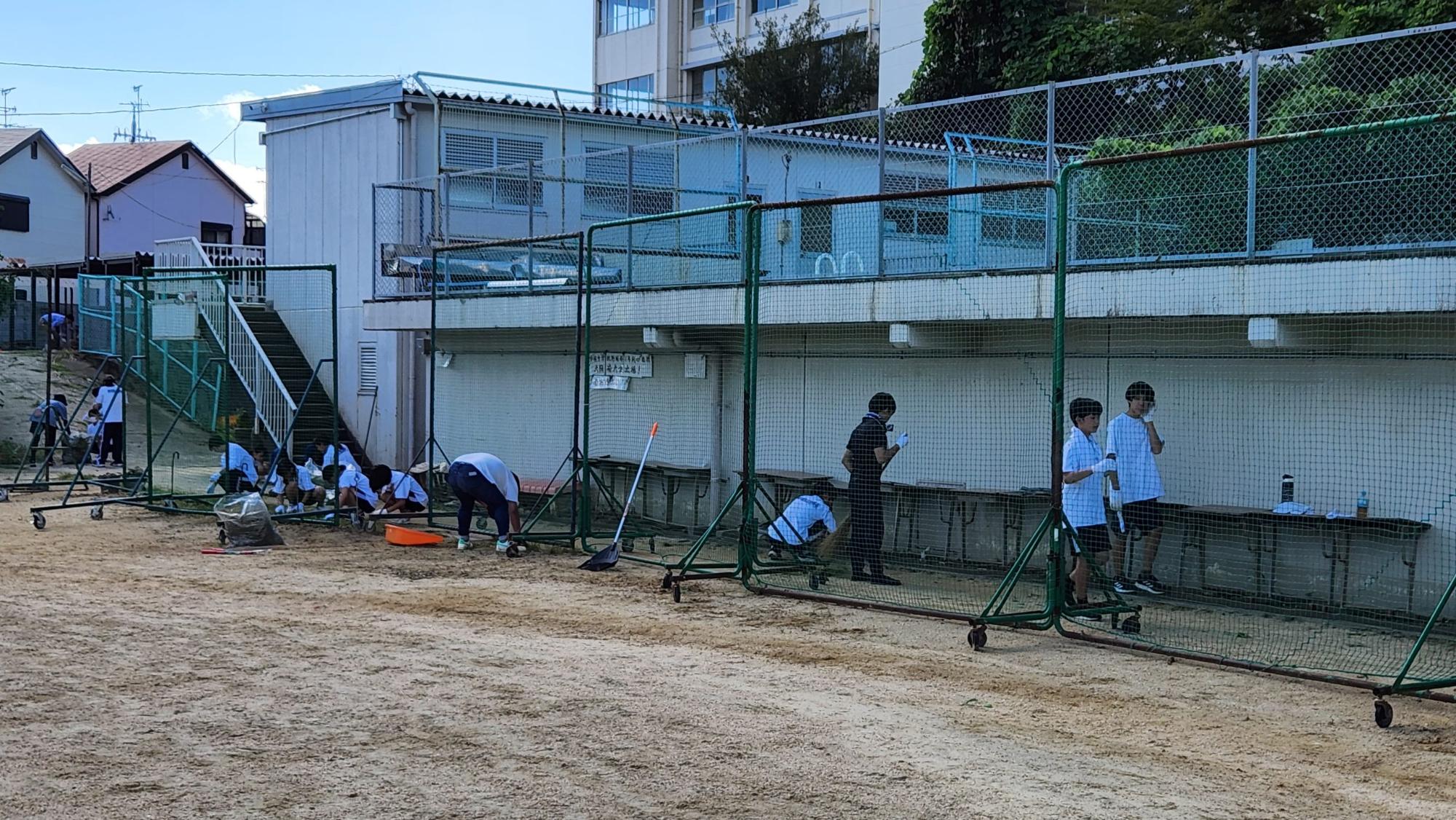 プールへ上がる階段下に設置された可動式のネットの下の草とりを行っているサポート隊の方々の写真