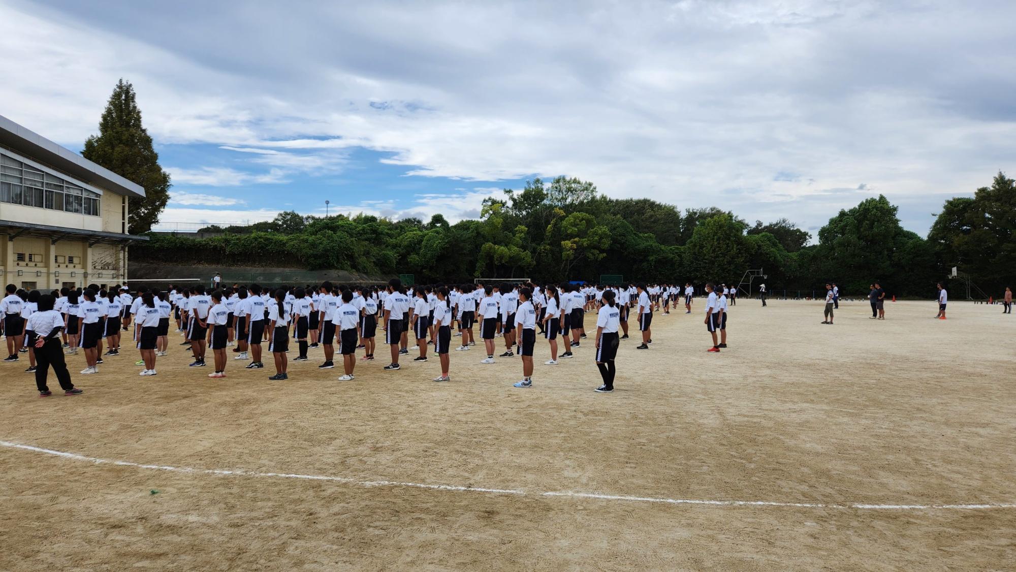 体育館前の運動場で体操着姿の生徒たちが並んでいる体育大会の練習の様子の写真