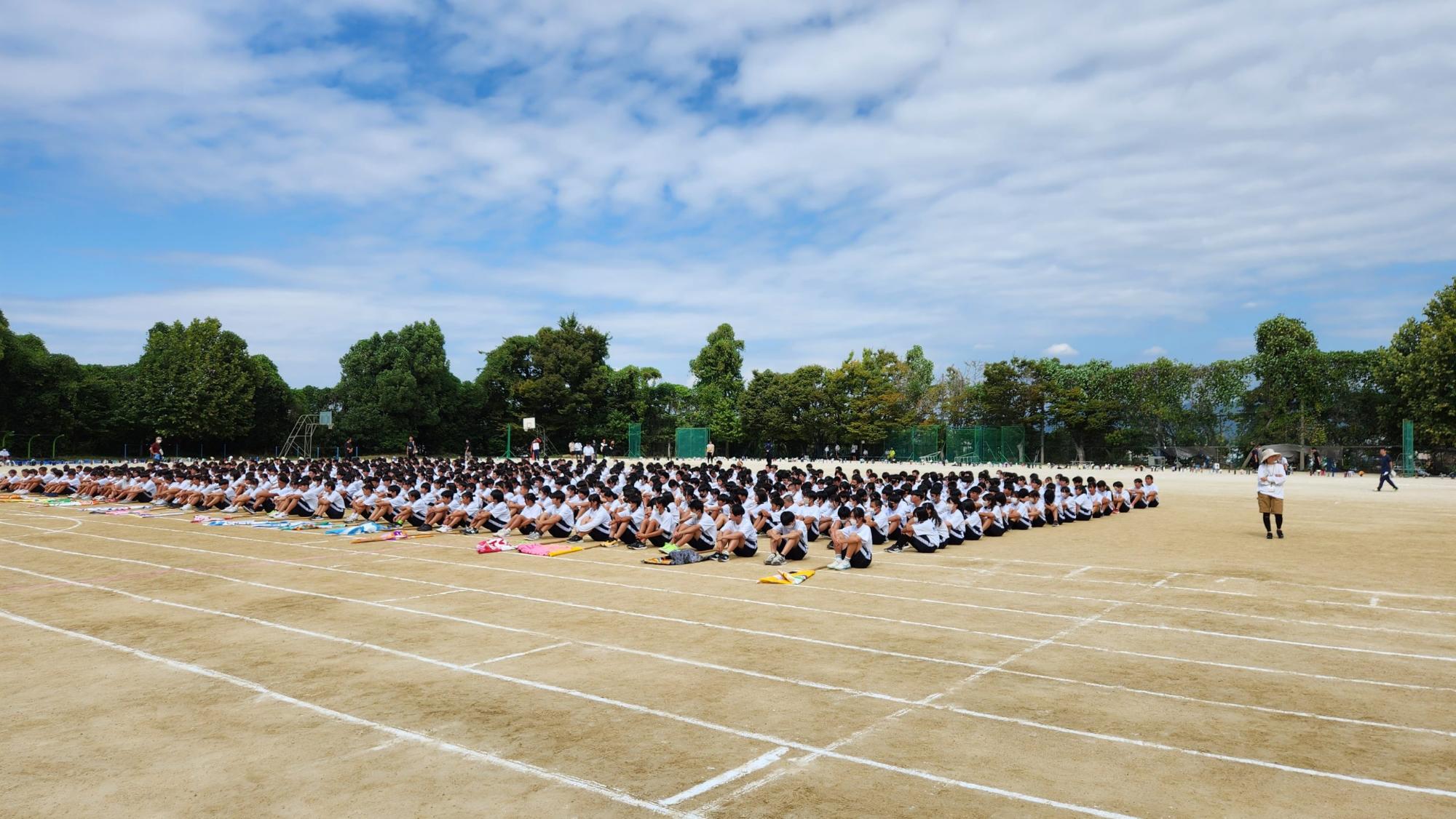 運動場の地面に置かれた団旗ごとに生徒たちが体育座りをしている体育大会の練習の様子の写真