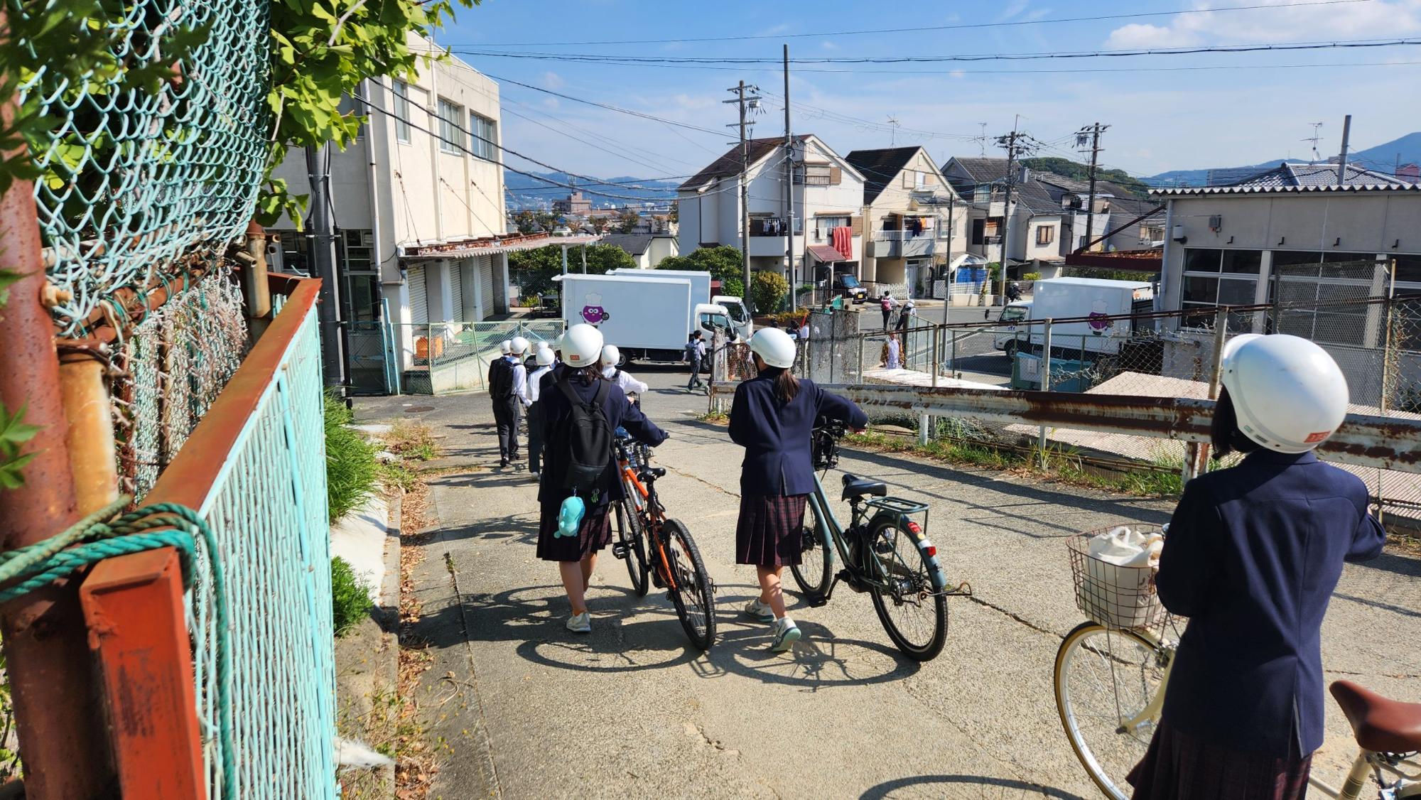 ヘルメットを被った生徒たちが自転車をひいて学校から出発して行く様子の写真