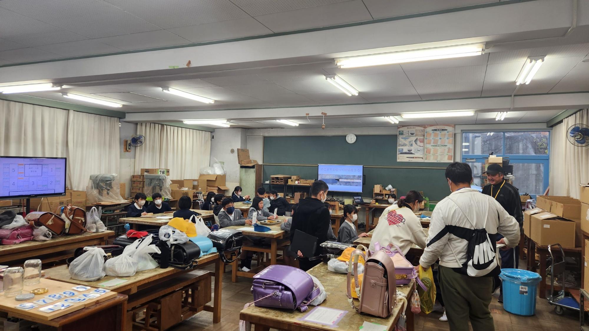 児童たちが4人掛けの机に4グループに分かれて座り、右手前の席に座っている同級生の様子を心配そうに見つめている体験授業の様子の写真